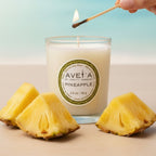 Bougie parfumée Tahiti Candles à l'ananas dans un pot en verre, allumée avec des morceaux d'ananas frais
