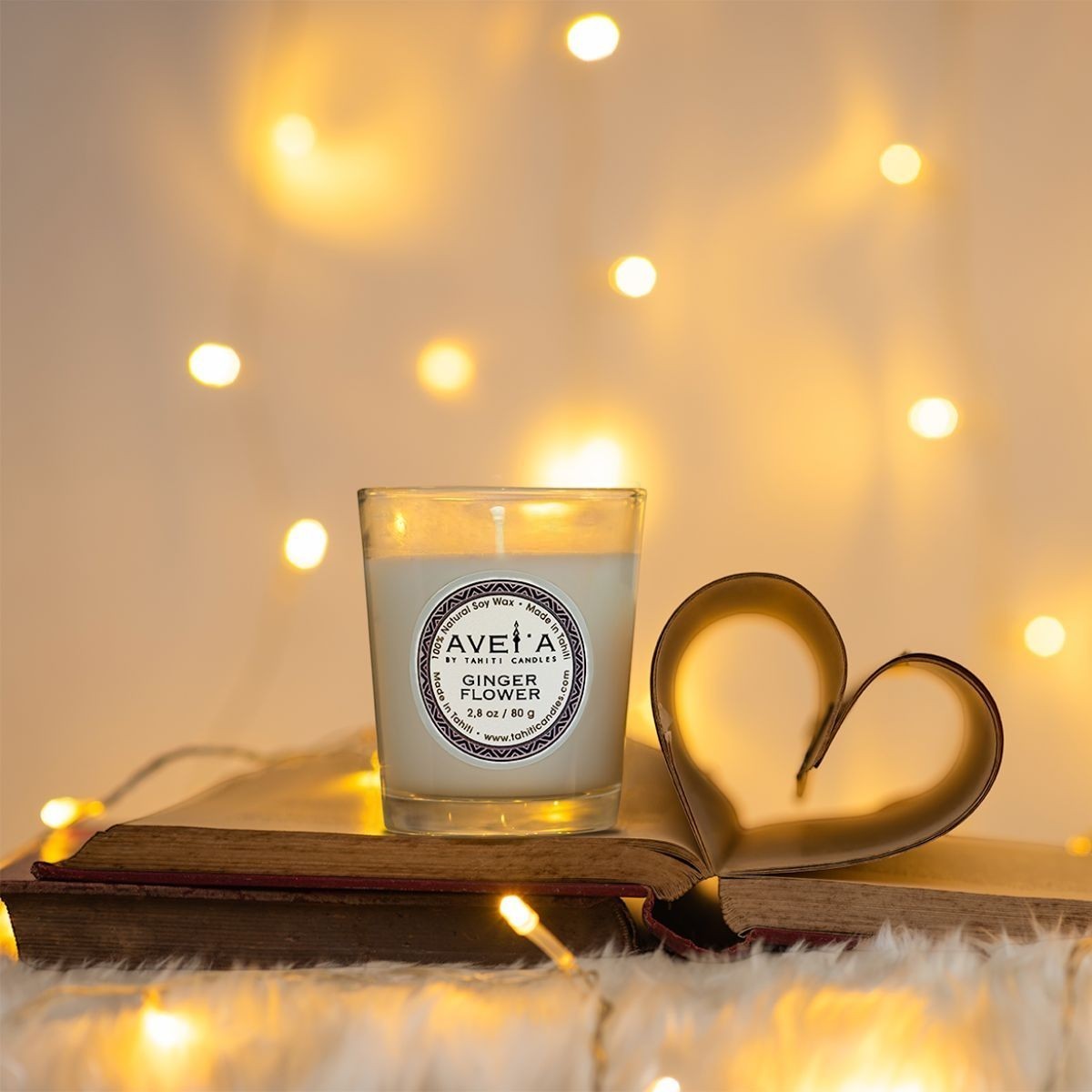 Bougie parfumée Tahiti Candles Ginger Flower 80g en cire naturelle sur un livre ouvert avec des lumières féeriques