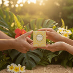 Tahiti Candles bougie parfumée Frangipani 80g dans son emballage jaune décoratif tenu par deux mains en extérieur