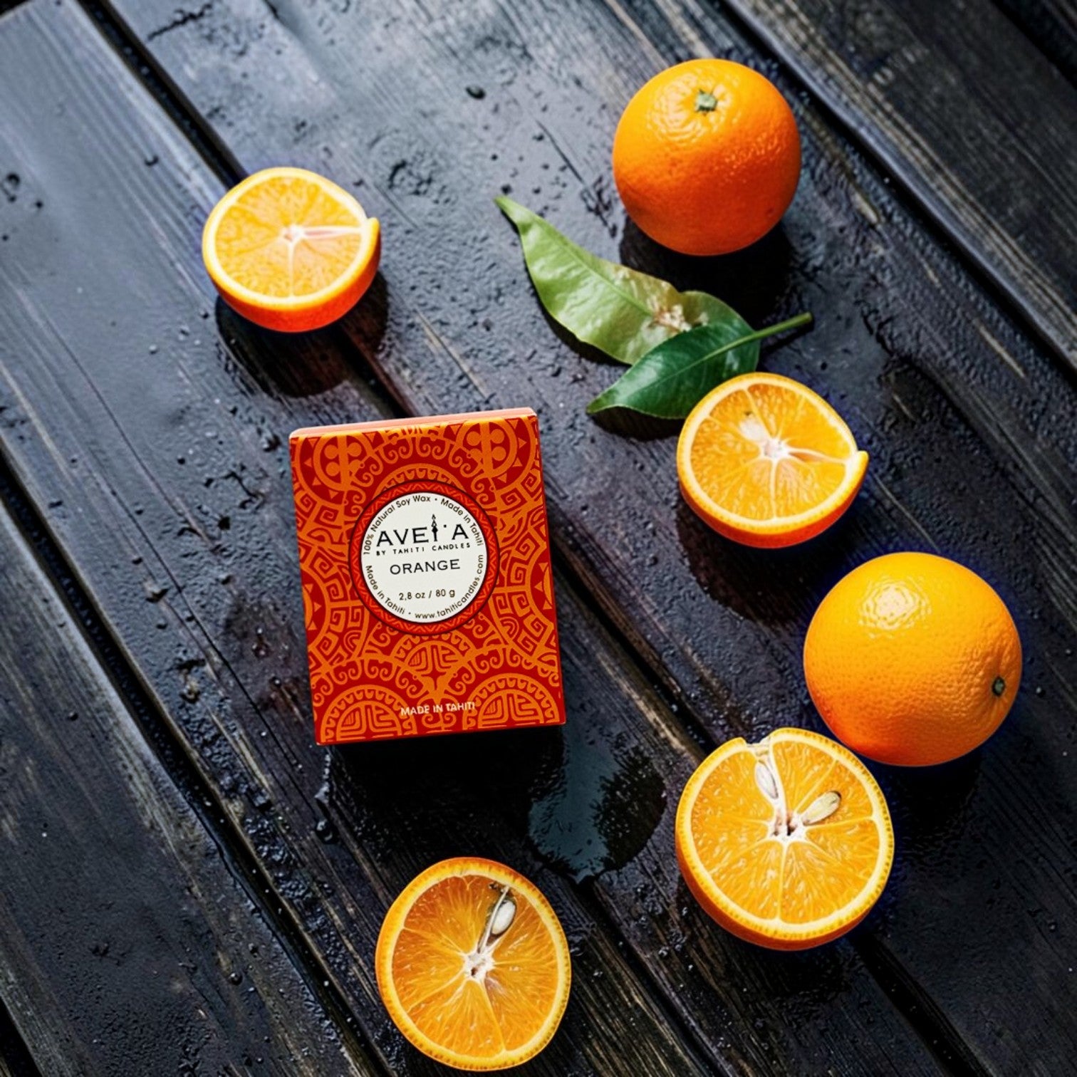 Bougie parfumée Tahiti Candles Orange 80g dans son emballage décoré, entourée d'oranges fraîches sur bois sombre