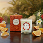 Bougie parfumée Tahiti Candles à l'orange dans un pot en verre avec sa boîte décorée sur une table tropicale