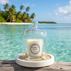 Bougie parfumée Tahiti Candles Sea Salt 80g sous cloche en verre sur un socle avec du sable, décor tropical en arrière-plan