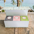 Coffret cadeau Tahiti Candles avec 3 bougies artisanales parfumées aux motifs polynésiens sur une terrasse en bois.